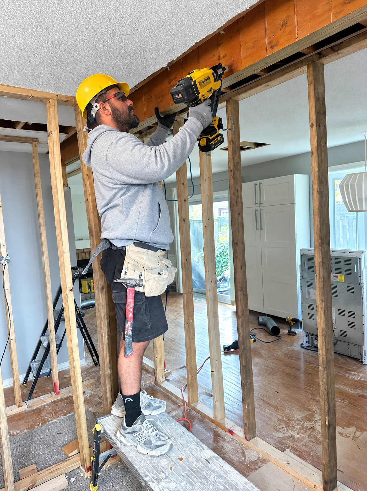 K1 Homes contractor in a yellow hard hat using a nailer on timber framing
